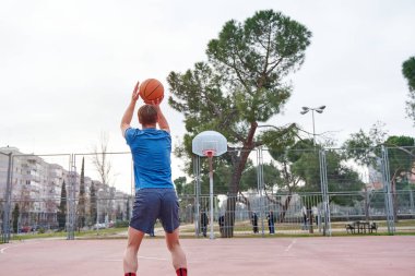 Basketbolcu atmadan önce sepete bakıyor. Genç adam top ve spor kıyafetleri ile.