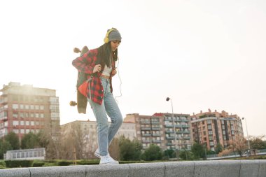Sırt çantası ve kaykayıyla şehirde yürüyen genç bir Latin. Venezuelalı İspanyol kadın spor yapıyor..