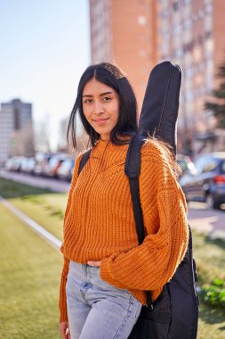 Gitar çantasıyla dışarıda poz veren güzel bir kadının portresi, Latin Amerikalı Etnik..