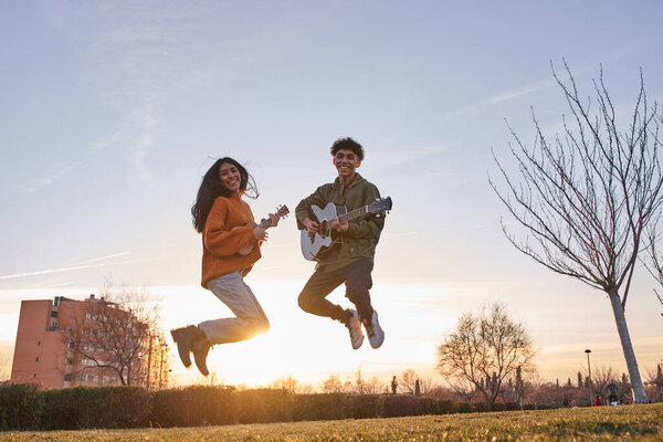 Счастливый молодой человек и молодая женщина прыгают с гитарой и укулеле над голубым небом