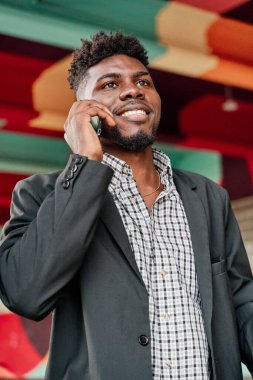 Renkli bir şehir geçmişi olan akıllı bir telefonla konuşan mutlu bir Afro-Amerikalının portresi.