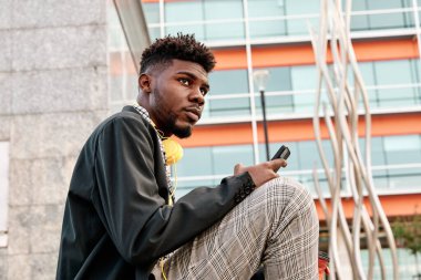 Genç Afro-Amerikalı adam cep telefonunu düşünceli bir şekilde kullanıyor.