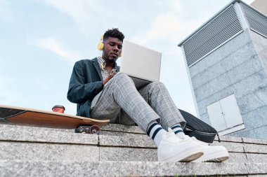 Dizüstü bilgisayarla uğraşırken kaykaylı genç bir Afro-Amerikalı yetişkinin görüntüsü