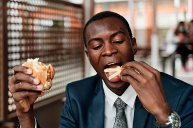 Fast food restoranında hamburger ve patates kızartması yiyen mutlu Afrikalı genç bir Amerikalı.