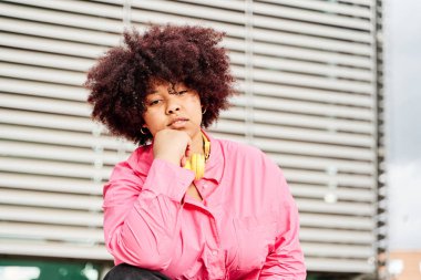 Kıvırcık saçlarıyla kameraya bakan Afrikalı Amerikalı bir kadının portresi. Eğik kadın pozu