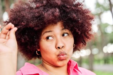 Genç, modern bir kız elinde bir tutam kıvırcık saç tutuyor. Afro-Amerikan kadın saçlarına mutlu bir şekilde bakıyor..