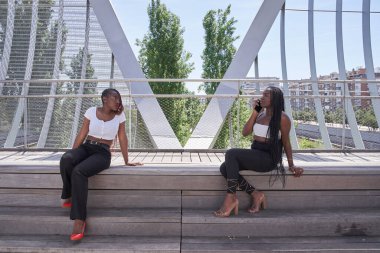 Parkta cep telefonuyla konuşan iki Afro-Amerikalı kadın.