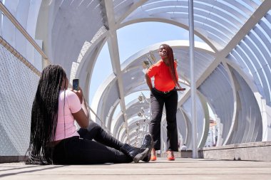 İki güzel Afro-Amerikalı kadın, fotoğraf makinesiyle birlikte ve eğlenirken biri akıllı telefonuyla arkadaşının dans edişinin fotoğrafını çekiyor. Genç mutlu en iyi arkadaşlar.