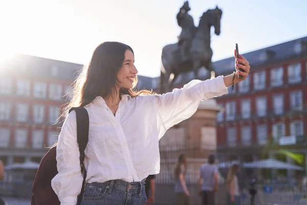 Madrid Plaza Belediye Başkanı 'nda İspanya Kralı 3. Felipe' nin Binicilik Anıtı önünde kameraya gülümseyen mutlu beyaz kadın selfie çekiyor.