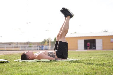 Pilates yaparken bacaklarını kaldıran bir adam çimlerin üzerinde yatar.