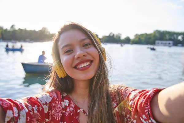 young latina taking a selfie with boats in the background. smiling tourist woman with white teeth and long hair.