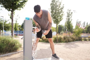 Antrenmandan sonra su şişesini dolduran dövmeli genç bir sporcu.