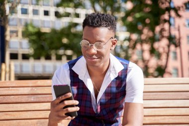 Genç Afro-Amerikan öğrenci akıllı telefon kullanıyor. Cep telefonuna bakan yakışıklı bir adam.