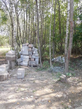Yeni, düzgünce paletlere istiflenmiş, aynı zamanda inşaat alanının yakınındaki ormanda taş taklit astarlı (hasarlı) beton bloklar ve köpük yalıtımı..