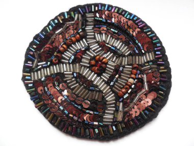 Parlak boncuklar ve pullardan yapılmış ev yapımı yuvarlak şekilli bir ürün. Koyu tonların yuvarlak kompozisyonu, fotoğrafın yazarının özelliği.