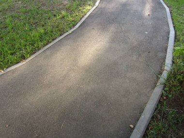 Parktaki yaya yolunun güzel bir virajı ya da yaya bölgesindeki bir cadde. Asfalt asfalt kaldırım elementleri tarafından çimlerden ayrılır..