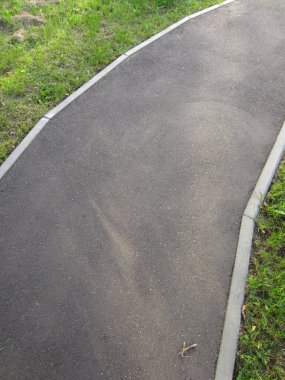 Parktaki yaya yolunun güzel bir virajı ya da yaya bölgesindeki bir cadde. Asfalt asfalt kaldırım elementleri tarafından çimlerden ayrılır..