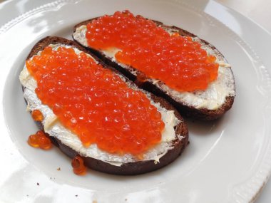 Lezzetli, lezzetli kırmızı havyar siyah ekmeğin üstünde tereyağlı, tabakta.