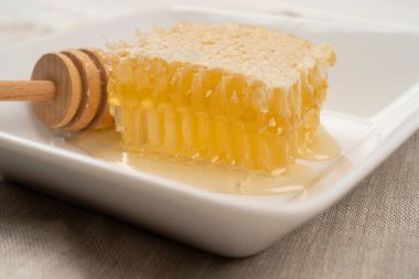 Keten zemin üzerinde dipper ve bal peteği olan tabaklar, manzarayı kapatın. Tabakta taze sıvı bal