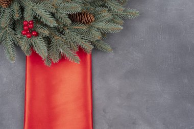 Noel ağacı dalları süslemeli ve kırmızı kış meyveli. Kırmızı ipek tekstil ve Noel çelengi ile kopyalama alanı