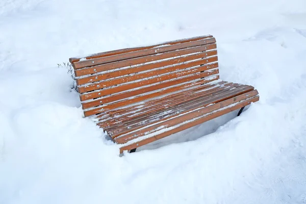 Parkta karla kaplı bir bank.