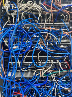 Communication rack with messy patch cables blue and grey close-up view