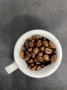 Kahve fincanındaki kahve çekirdekleri ön plana seçici bir şekilde odaklanmış.