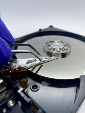 Eldivenli eldeki kıskaç, yakın plan yansımalı bir disk plakasına dokunuyor.