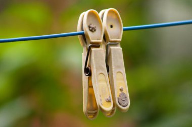 Close-up of two yellow clothes hooks hanging on a blue wire with green blurred background
