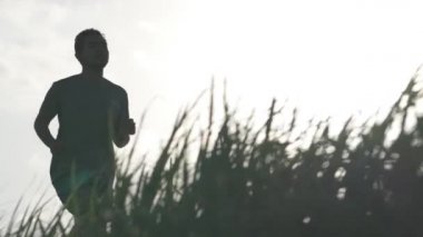 Three healthy active Asian Indonesian Men Running in Slow Motion on Beautiful Outdoor Nature Green Grass Rice Field Jogging Track During Sunset - Bali Indonesia