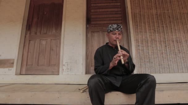 インドネシアのカンプン 伝統的な黒の衣装を着た男が村でサンデンフルートを演奏 — ストック動画