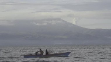 Fisherman on Small Boat in The Sea Ocean with Mountain on The Background Cloudy Day