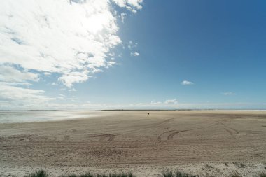 Geniş kumlu plajlar, mavi gökyüzü ve bulutlar.