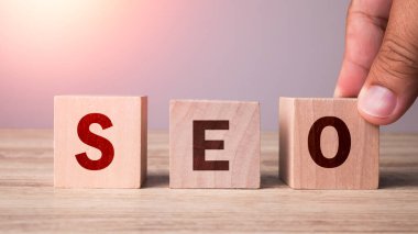 Close up Hand putting wooden cube block shape to SEO text on wood table background. Search Engine Optimization, Advertising, Idea, Strategy, marketing, Keyword and Content concept