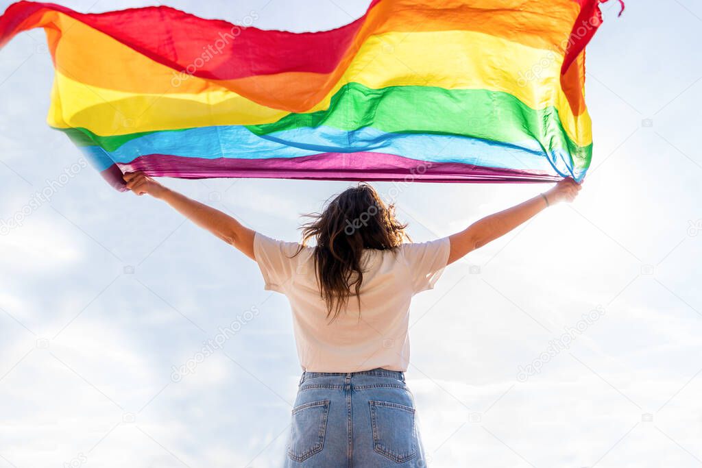Young woman waving LGBTQ flag staring at the sun.