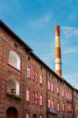 Polonya 'nın Katowice kentindeki geleneksel Nikiszowiec semtinde binanın ön cephesi. Kırmızıya boyanmış pencereli eski tuğla evler. Arka planda fabrika bacası. 