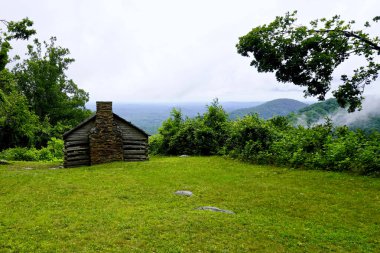 Log settler's cabin built by W. J. Trail at the Smart View Recreation Area on the Blue Ridge Parkway. Low rolling clouds on Appalachian Mountains. Pioneer dwelling of one room built in early 1890s.