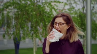 Genç bayan yürüyor ve yemek yiyor. Foo ile mutluyum. Park 'ta Sokak Yemeği. Aç iş kadını..