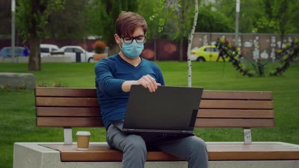 公園で働いてる 若い男性がノートパソコンを開きます入力は インターネットドリンクコーヒーをサーフ電子メールを書き込み — ストック動画