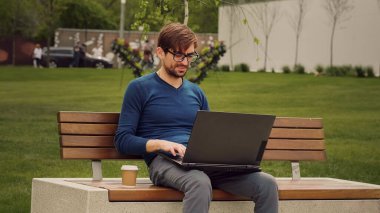 Başarılı bir meşgul Kafkasyalı genç afro erkek öğrenci kablosuz kulaklıklar takan serbest çalışan erkek programcı şehirde terasta oturmuş bilgisayarlı sohbet yazarak internetten e-öğreniyor.