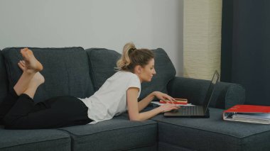 Dizüstü bilgisayarda yazan konsantre genç bir kadın. Başarılı bir proje tasarla. Serbest çalışan biri. Kanepede oturup çok çalışmak..