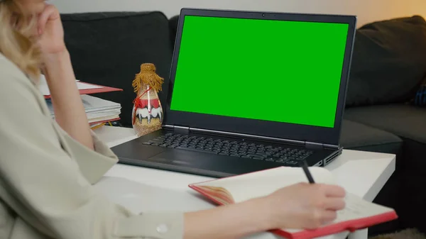 Renkli Laptop Ekranı ile Yeşil Ekranı kapat. Masada oturan iş kadını dizüstü bilgisayarından notlar alır, ekrana bakar ve sonra da deftere bakar. Ofisin içinde çalışıyorum..