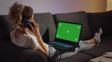 Kanepede oturan bir kadın dizüstü bilgisayarda çalışıyor Yeşil Ekran Krom Anahtarı 'nı kurgulayıp telefonla konuşuyor. PC kullanan serbest çalışan, sosyal medya reklamları için internette gezinen.