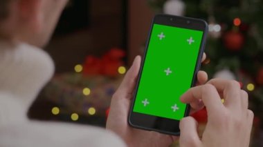 Yakın çekim Yeşil Ekran Krom Anahtar Akıllı Telefon evde, Noel 'de erkeklerin elinde. Adam içerik kaydırma aygıtı ekranını izliyor. Modern teknoloji ve bilgi kavramı.