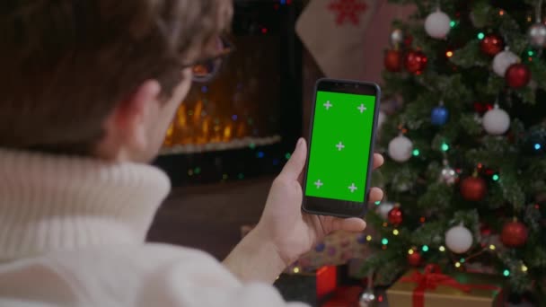 英俊男子手持智能手机与绿色屏幕在圣诞背景与礼物 用Chroma键关闭移动电话 利用技术实现Internet Digitzation — 图库视频影像
