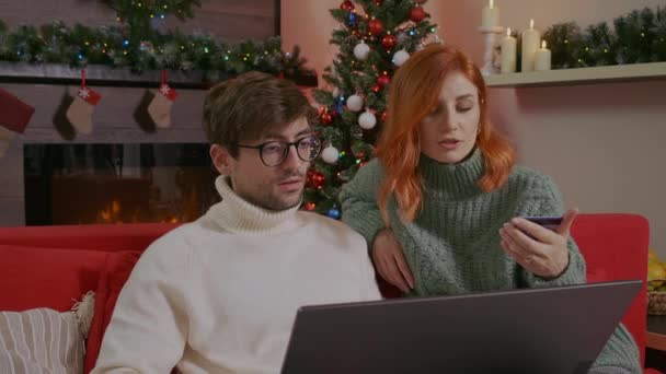 Young couple makes online purchase through Internet store using laptop, buy Christmas presents doing online ecommerce shopping purchase payment. Christmas Gifts purchase online concept. — Stock Footage Young Couple Makes Online Purchase Internet Store Using Laptop Buy Stock Footage