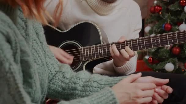 Man is playing Christmas song on acoustic guitar near decorated Christmas tree. Happy family Celebrating of New Year 2021 and Merry Christmas. Happy friends having fun singing on holidays. — Stock Footage Man Playing Christmas Song Acoustic Guitar Decorated Christmas Tree Happy Royalty Free Stock Footage