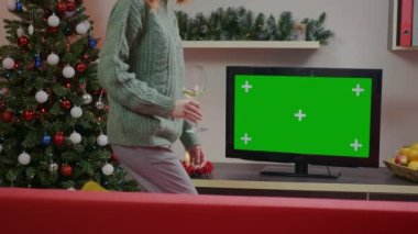 Noel tatili konsepti. Güzel kadınlar oturma odasında kanepede otururken Green Chroma Key TV izleyip bir bardak şarap içiyorlar. Rahatlatıcı kış tatili.