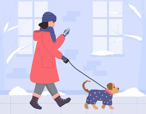 一个穿着保暖外套 头戴帽子 戴着手套的女孩带着一只狗走过冬日街 看着电话 一只穿着蓝色连衣裙的小狗 平面样式的矢量图解 — 图库矢量图片