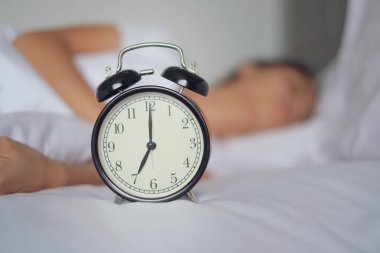Yatakta uyuyan bir kadın çalar saati kapatır ve sabah uyanır, seçici bir şekilde odaklanır.
